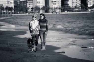 Mutlu kıdemli anne yetişkin kızı ve Alman shepard köpek vakit birlikte günbatımı ışık kumsalda mutlu aile anlarda evde beslenen hayvan hayvanlar yürürken köpek dostu Turizm ve emeklilik faydaları.