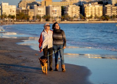 Mutlu kıdemli anne yetişkin kızı ve Alman shepard köpek vakit birlikte günbatımı ışık kumsalda mutlu aile anlarda evde beslenen hayvan hayvanlar yürürken köpek dostu Turizm ve emeklilik faydaları.