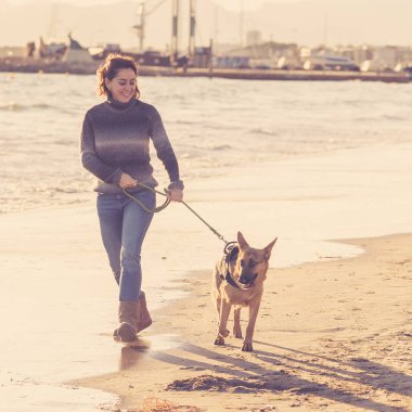 Güzel yetişkin kadın ve evde beslenen hayvan Alman shepard köpek arkadaşlık faydaları hayvanların köpeklerin yaşam tarzı ve köpek dostu Turizm Eğitim öğleden sonra batımında sahilde kıyı deniz okyanus yürüyen.