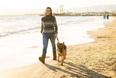 Güzel yetişkin kadın ve evde beslenen hayvan Alman shepard köpek arkadaşlık faydaları hayvanların köpeklerin yaşam tarzı ve köpek dostu Turizm Eğitim öğleden sonra batımında sahilde kıyı deniz okyanus yürüyen.