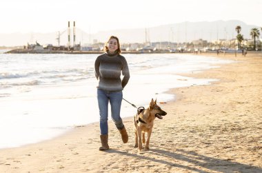 Güzel yetişkin kadın ve evde beslenen hayvan Alman shepard köpek arkadaşlık faydaları hayvanların köpeklerin yaşam tarzı ve köpek dostu Turizm Eğitim öğleden sonra batımında sahilde kıyı deniz okyanus yürüyen.