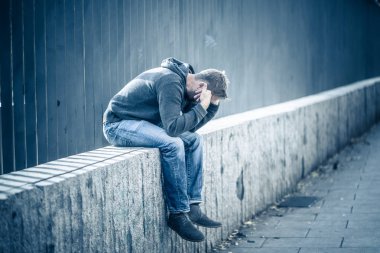 Genç çekici adam acı depresyon stres tek başına oturmak ve üzücü duygu endişeli ve işsizlik ruh sağlığı uyuşturucu ve alkol bağımlılığı kavram yalnız sokakta.