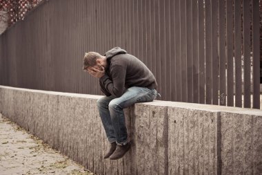 Genç çekici adam acı depresyon stres tek başına oturmak ve üzücü duygu endişeli ve işsizlik ruh sağlığı uyuşturucu ve alkol bağımlılığı kavram yalnız sokakta.