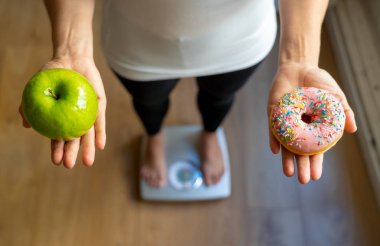Kadının elleri apple ve vücut ağırlığı beslenme Sağlık Bakımı Diyet ve günaha kavram ölçme sırasında sağlıklı sağlıksız yiyecek tatlı arasında seçim yapma halka tutarak ölçekte yakın çekim.