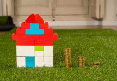 Kavramsal görüntü oyuncak evi ve yeşil çim alan üst sikkelerinde yığınları görüntülemek ve uzay Emlak Yatırım kaydetme ve ev ipotek satın alma gayrimenkul içinde kopyalama ve sigorta ve kavram banka kredisi.