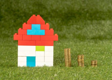 Kavramsal görüntü oyuncak evi ve yeşil çim alan üst sikkelerinde yığınları görüntülemek ve uzay Emlak Yatırım kaydetme ve ev ipotek satın alma gayrimenkul içinde kopyalama ve sigorta ve kavram banka kredisi.