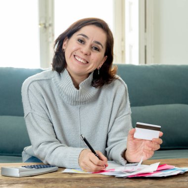 Genç çekici latin iş kadını mutlu ve memnun kredi borç kart avantajları ve kullanım ve muhasebe maliyeti, ücretleri, vergiler ve ipotek hesap makinesi evde kanepe ile seyir .