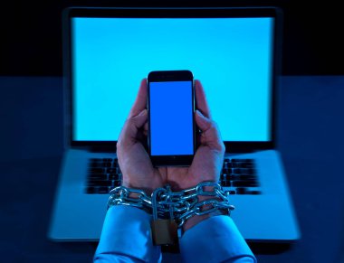 Genç adam bağlı ve akıllı bilek üzerinde asma kilit ile demir metalik zinciriyle kilitli cep telefonu eller bond bağımlısı telefon internet ve sosyal medya bağımlılık ve Teknoloji kurbanı kavramı köle.