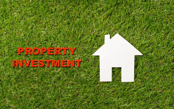 Conceptual picture of white house and Property Investment text written on green grass field top view in Housing Market Real estate Saving and buying a home mortgage and loan banking concept.
