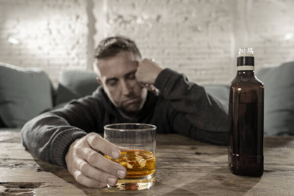 Пьяный молодой человек, употребляющий алкоголь дома, падая одиноким, подавленным и больным, держит стакан виски в белом и черном и пьет в цвете в концепции алкогольной зависимости
.