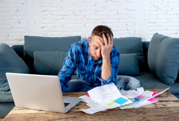 Worried and stressed man calculating bills tax expenses and counting home and business finances sitting on the couch at home in paying off debts and domestic bills and financial problems concept.