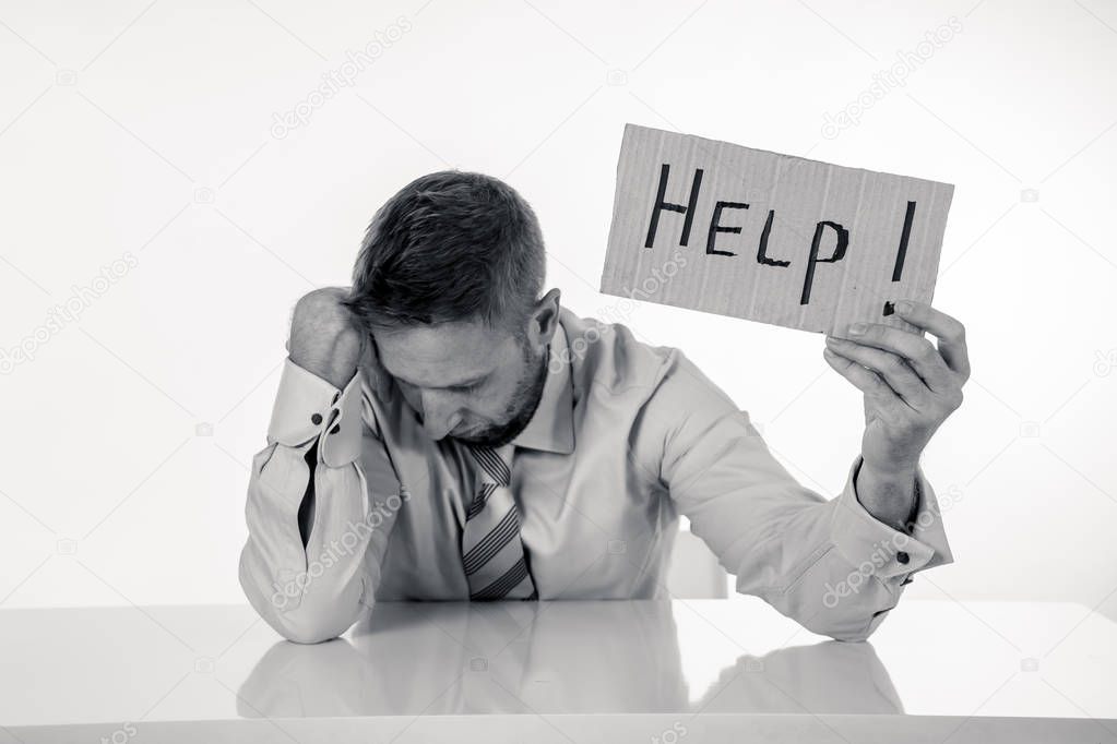Young attractive frustrated and tired caucasian businessman holding help sign message exhausted and sad under pressure and stress isolated on white in unemployment depression and overwork concept.