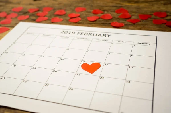 Close up of focused red heart on Saint valentines day on out of focus calendar and hearts in blur romantic light in getting ready for Valentines date, Love celebration, dreams and romantic concept.
