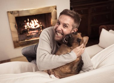 Mutluluk Dostluk Aşk Arkadaşlık ve evcil hayvanların faydaları kış günü rahat evde şömine önünde birlikte oynayan köpek alman çoban sarılma gülümseyen adam güzel portre.