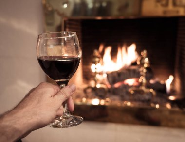 Adam tutarak ve rahatlatıcı ve sakin an evde kış tatil tatil, yılbaşı ya da boş zaman kavramı içinde zevk açık ahşap yangın yeri tarafından kırmızı şarap cam içme yakın çekim.