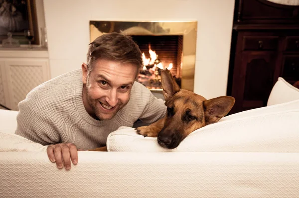 Beautiful portrait of smiling man hugging dog german shepherd playing together in front of fireplace at cozy home in winter day in happiness Friendship Love Companionship and benefits of pets animals.