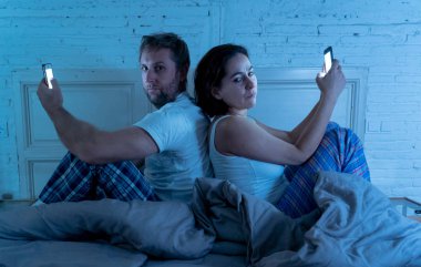 Üzgün bir adam ve kadın evli çift birbirlerine yabancı ilişki ve iletişim sorunları ve internet sosyal ağ bağımlılığı olarak görmezden geceleri yatakta akıllı cep telefonlarını kullanarak.
