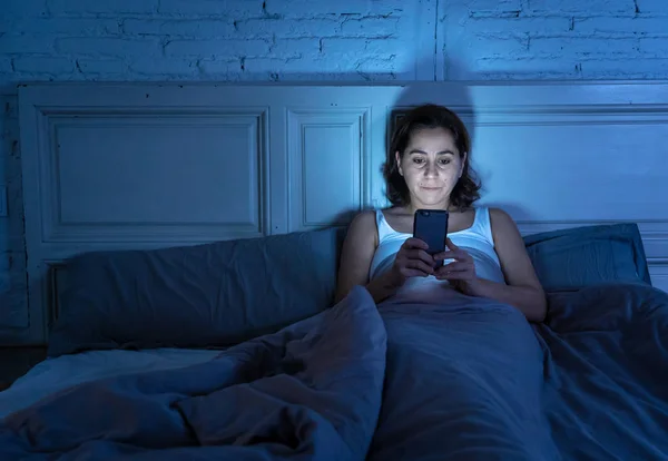 Addicted young beautiful woman chatting and surfing on the internet using her smart phone sleepy bored and tired late at night in Internet, Mobile addiction and insomnia concept.