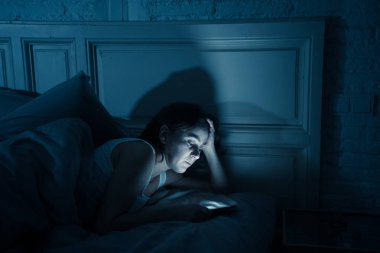 Genç çekici kadın uyanık geç gece karanlık bir yatak odasında yatakta yalan akıllı telefon kullanarak. Sohbet ve internet bağımlılığı, mobil istismar ve uykusuzluk kavramı iletileri göndermek için mobil kullanma