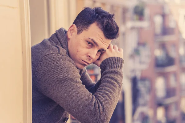 Sad unhappy depressed young man crying and suicidal feeling desperate, isolated and worthless staring down the street on home balcony In People Depression and Mental Health concept. Urban background.