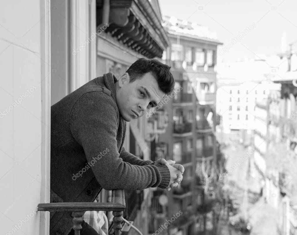 Sad unhappy depressed young man crying and suicidal feeling desperate, isolated and worthless staring down the street on home balcony In People Depression and Mental Health concept. Urban background.