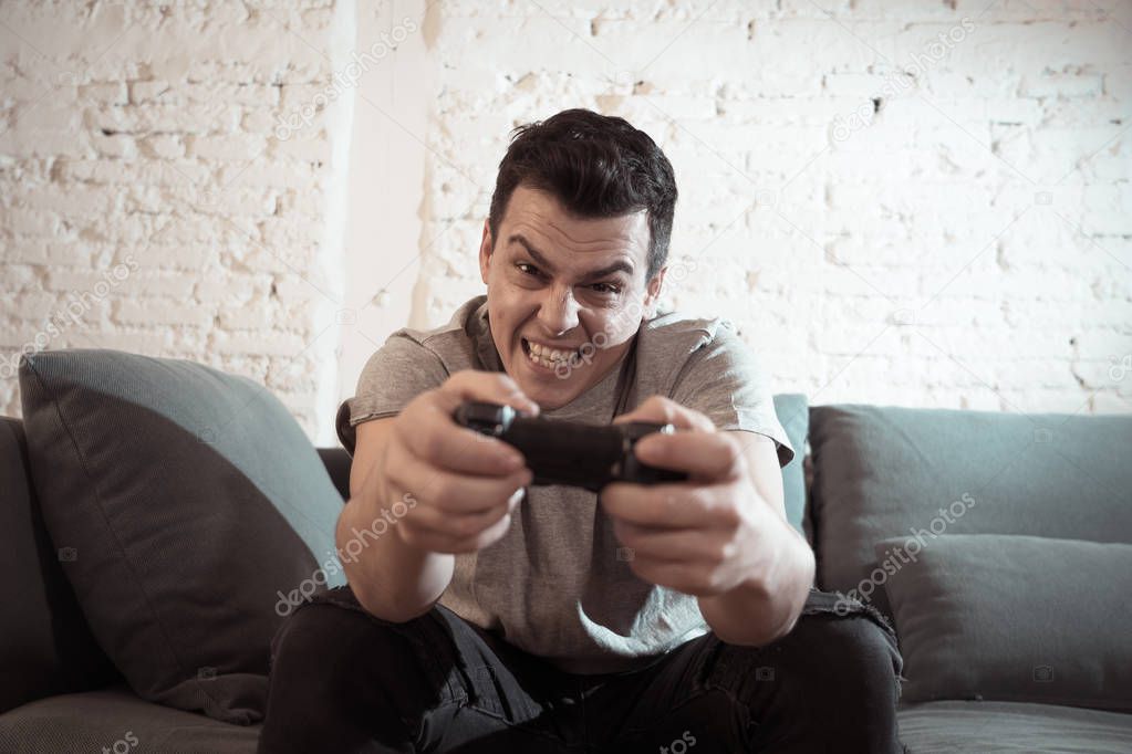 Portrait of young student man spending time playing video games using wireless remote joystick with freak intense happy face having fun in Male game addiction to console play station and video.