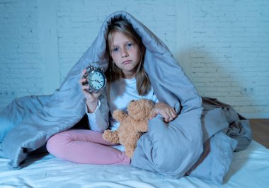 Cute sleepless little girl sitting on bed looking sad and tired having sleeping troubles staying asleep at night or waking too early in the morning in Insomnia Anxiety Sleep Disorders in children. clipart