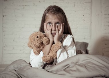 Korku içinde onun oyuncak Çocuk kabus hayal ve psikolojik sıkıntı konsept yatak odasında karanlıkta canavarlar korkuyor tutan elleriyle yüzünü kaplayan yatakta oturmuş korkmuş küçük bir kız.