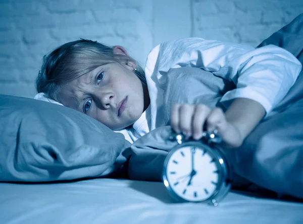 Sweet sleepless little girl stressed sad and angry in bed looking at alarm clock having to wake up but feeling sleepless in Troubles staying asleep Sleep disorder and Children Insomnia concept.