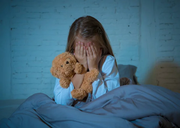 害怕的小女孩坐在床上 用双手抱着她的泰迪熊捂着她的脸 害怕在黑暗中害怕怪物在卧室里的儿童噩梦想象和心理困扰的概念 — 图库照片