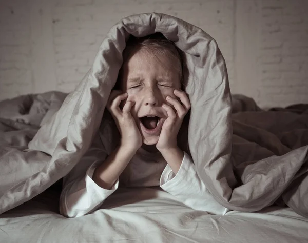 Cute asleep girl screaming and crying after frightening or upsetting dream covering herself with blanket in bed at night in mood dramatic lighting in Sleep terrors Nightmares and Sleeping disorders.