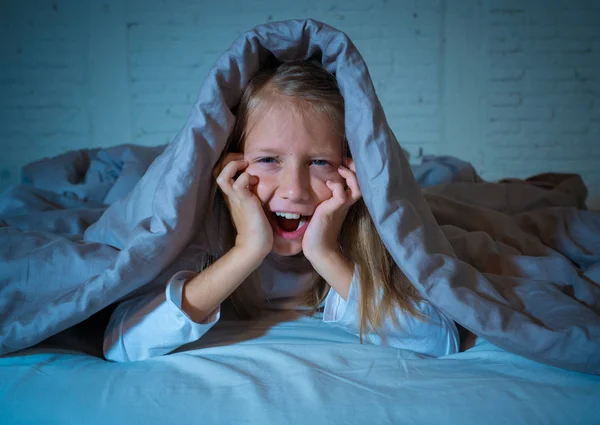 Cute asleep girl screaming and crying after frightening or upsetting dream covering herself with blanket in bed at night in mood dramatic lighting in Sleep terrors Nightmares and Sleeping disorders.