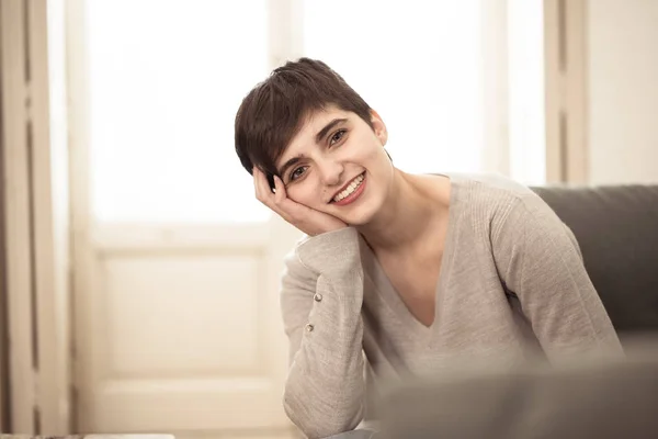 Life style woman indoor portrait of Stunning short haired young woman with beautiful smile sitting on sofa at home with beautiful light. In People youth and leisure concept.