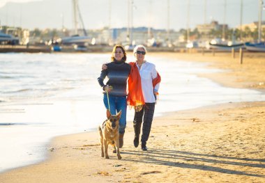 Mutlu kıdemli anne yetişkin kızı ve Alman shepard köpek vakit birlikte günbatımı ışık kumsalda mutlu aile anlarda evde beslenen hayvan hayvanlar yürürken köpek dostu Turizm ve emeklilik faydaları.