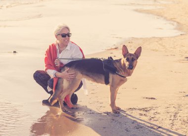 Güzel dul yaşlı kadın onun Alman shepard onun arkadaşı zevk köpek ve aşk ile sahilde günbatımı hayvan faydaları tutma aktif emeklilik yaşam tarzı oynayan ve dostu Turizm köpek.