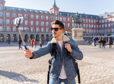 Çekici genç beyaz turistik öğrenci adam mutlu ve heyecanlı bir selfie akıllı cep telefonu ile Plaza Mayor, Madrid, İspanya alarak eğleniyor. Seyahat, tatil, tatil Europe kavramı çevresinde.