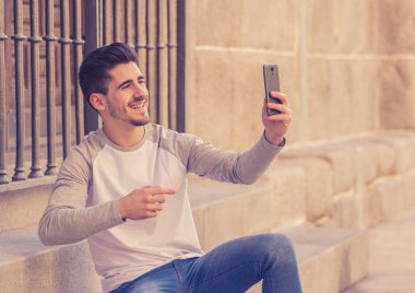 Trendy genç adam akıllı cep telefonunda tatil günlerinde Avrupa şehri sokak veya üniversite kampüs dışında bir selfie alarak heyecanlı. Bayram ve teknoloji, bağlantı ve sosyal medya kavramı.