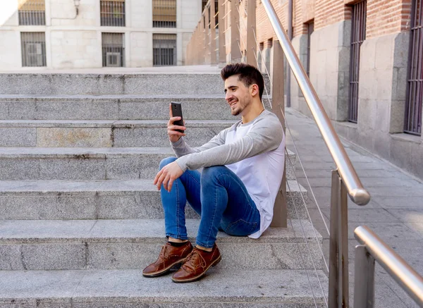 若い魅力的な大学キャンパスや街の階段のスマートな携帯電話で友人とのおしゃべりと話して幸せな 代の男 通信技術のインターネットとヨーロッパのまわりの旅行 — ストック写真