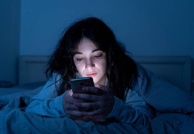 Uykusuz seyir yatakta cep telefonu ve gece geç saatlerde internet bağımlısı çekici latin kadın