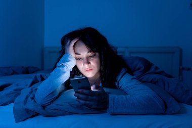 Uykusuz seyir yatakta cep telefonu ve gece geç saatlerde internet bağımlısı çekici latin kadın