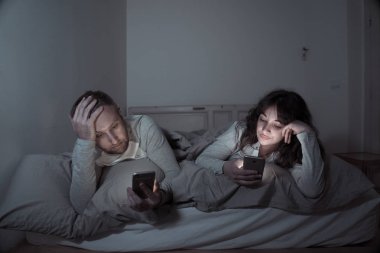 Akıllı telefonlarda geceleri yatakta genç sıkılmış çift portresi yaşam tarzı Oyunlar, sosyal medya, birbirimizi görmezden apps ile takıntılı. İlişki iletişim sorunları ve telefonu bağımlılığı konsepti.