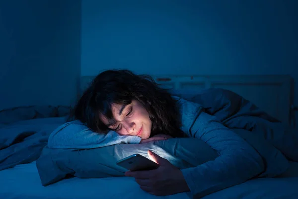 Mulher latina atraente viciada em telefone celular e internet no final da noite na cama olhando sem dormir — Fotografia de Stock