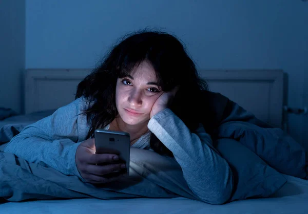 Attractive latin woman addicted to mobile phone and internet late at nigh in bed looking sleepless — Stock Photo, Image