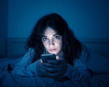 Sohbet ve akıllı telefonunu uykulu, bıkkın ve yorgun gece geç saatlerde kullanarak internette sörf bağımlısı genç kadın. Dramatik koyu. Internet, mobil bağımlılığı ve uykusuzluk kavramı.