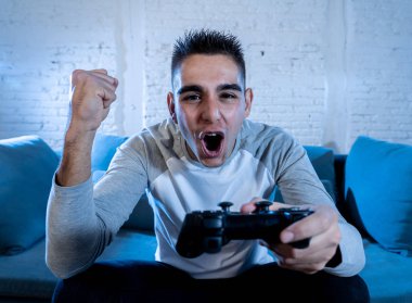 Genç adam eğleniyor portresi kazanan kutluyor ucube yoğun mutlu yüz ile kablosuz uzaktan joystick kullanarak video oyunları oynamak. Konsol erkek oyun bağımlılığı istasyonu ve video oynamak.