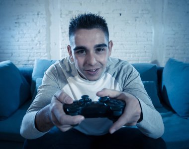 Ucube yoğun bağımlısı yüz erkek oyun bağımlılığı konsol oyun istasyonu ve video having oyunculuk ile kablosuz uzaktan joystick kullanarak gece video oyunları oynarken genç öğrenci adam portresi.