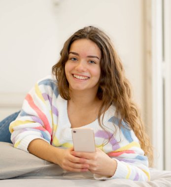 Sosyal medya uygulamaları sohbet veya online kişi, yaşam tarzı, iletişim ve yeni teknoloji kavramı evde yatakta yatan oyun cep telefonuna mesaj gönderme mutlu güzel kız.