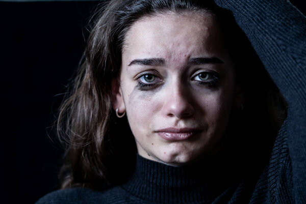 Dramatic closeup portrait of young scared, depressed girl crying alone, feeling hopeless suffering from harassment or domestic violence. Stop child abuse and neglect. Social campaign concept.