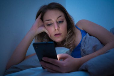 Sohbet ve telefon bağımlılığı ve teknoloji aşırı kavramı gece geç saatlerde akıllı telefonunu uykulu, donuk ve yorgun kullanarak Internet sörf bağımlısı genç güzel kadın yatakta,.