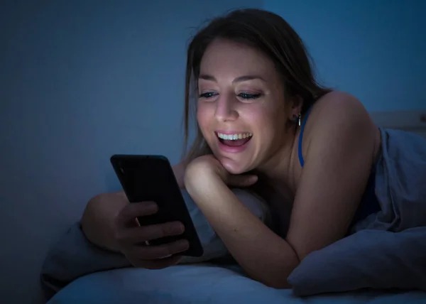幸せな若い美しい女の子と話して彼女のスマート フォンを使用してインターネット上でサーフィンします 明るく楽しい女性ビデオ チャットで夜遅くリラックスし カジュアルな気分 携帯電話依存症の概念 — ストック写真